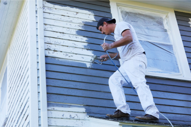 Exterior House Painter up high on a home with a spray gun